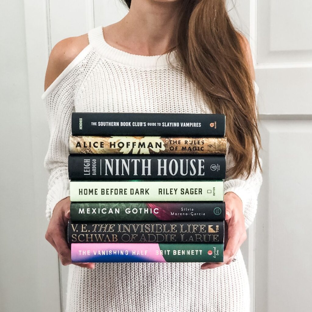 a woman in a white dress holding a stack of hardcover books