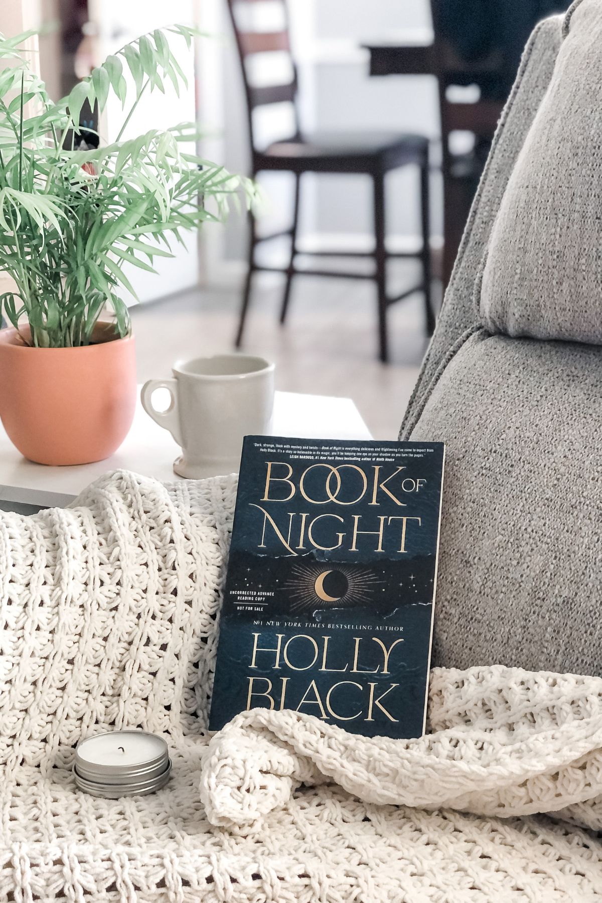 grey reading chair set up for read-a-thon with white blanket, book, and mug of coffee