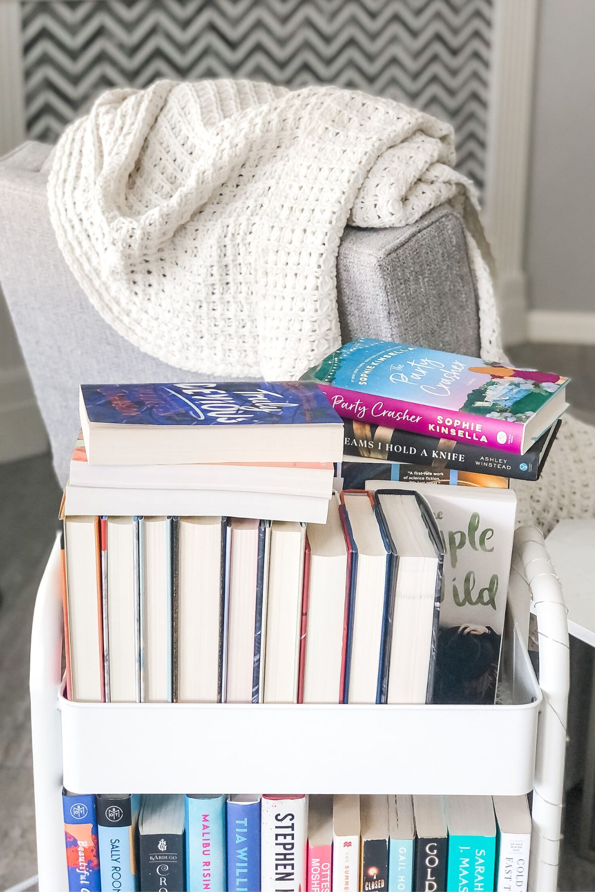 book cart with piles of books next to a comfy reading chair