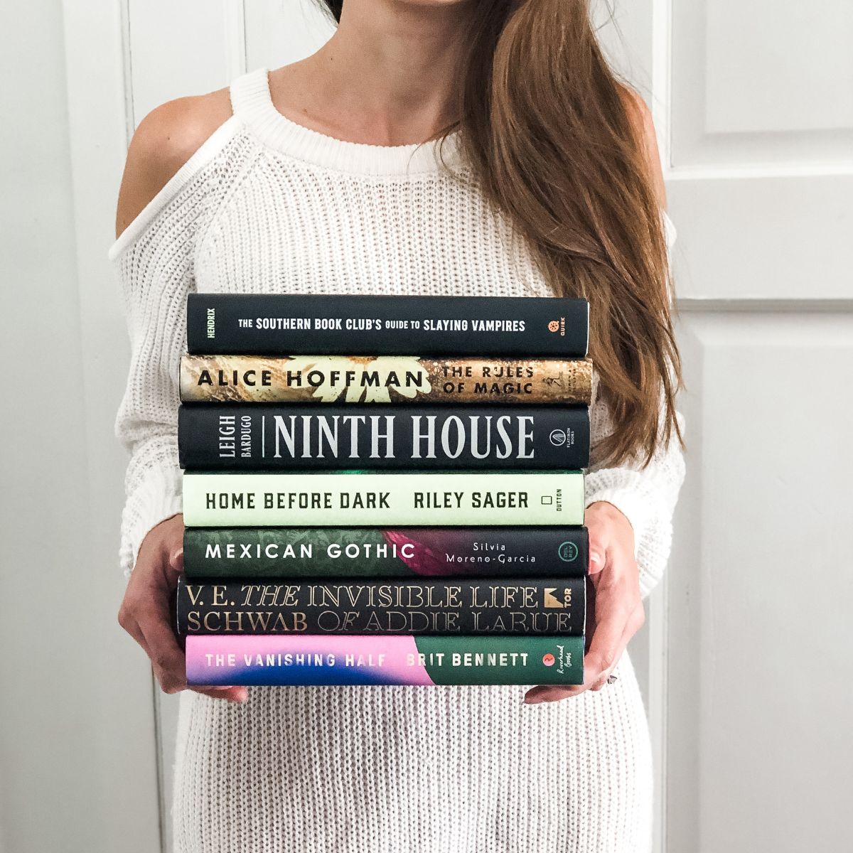 a woman wearing a white sweater holding a stack of books