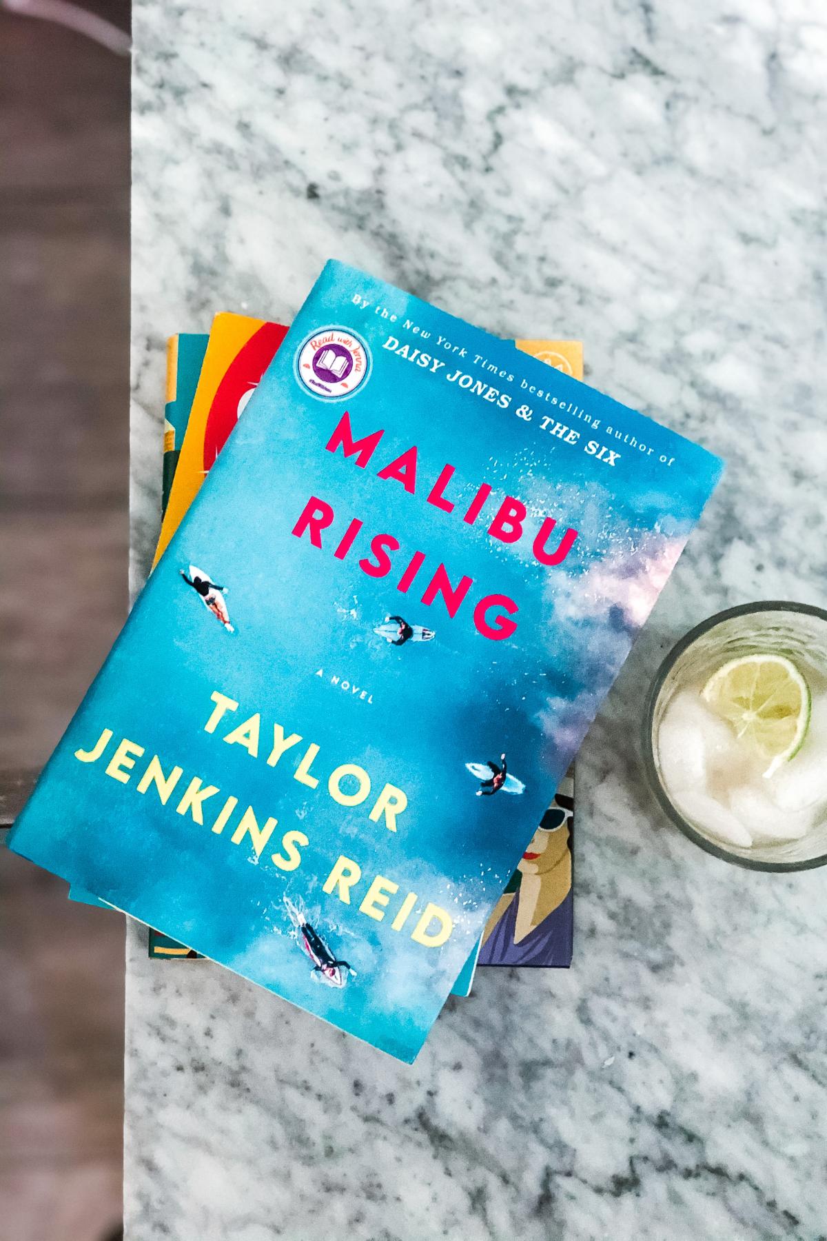 Malibu Rising hardcover book next to a drink with lime