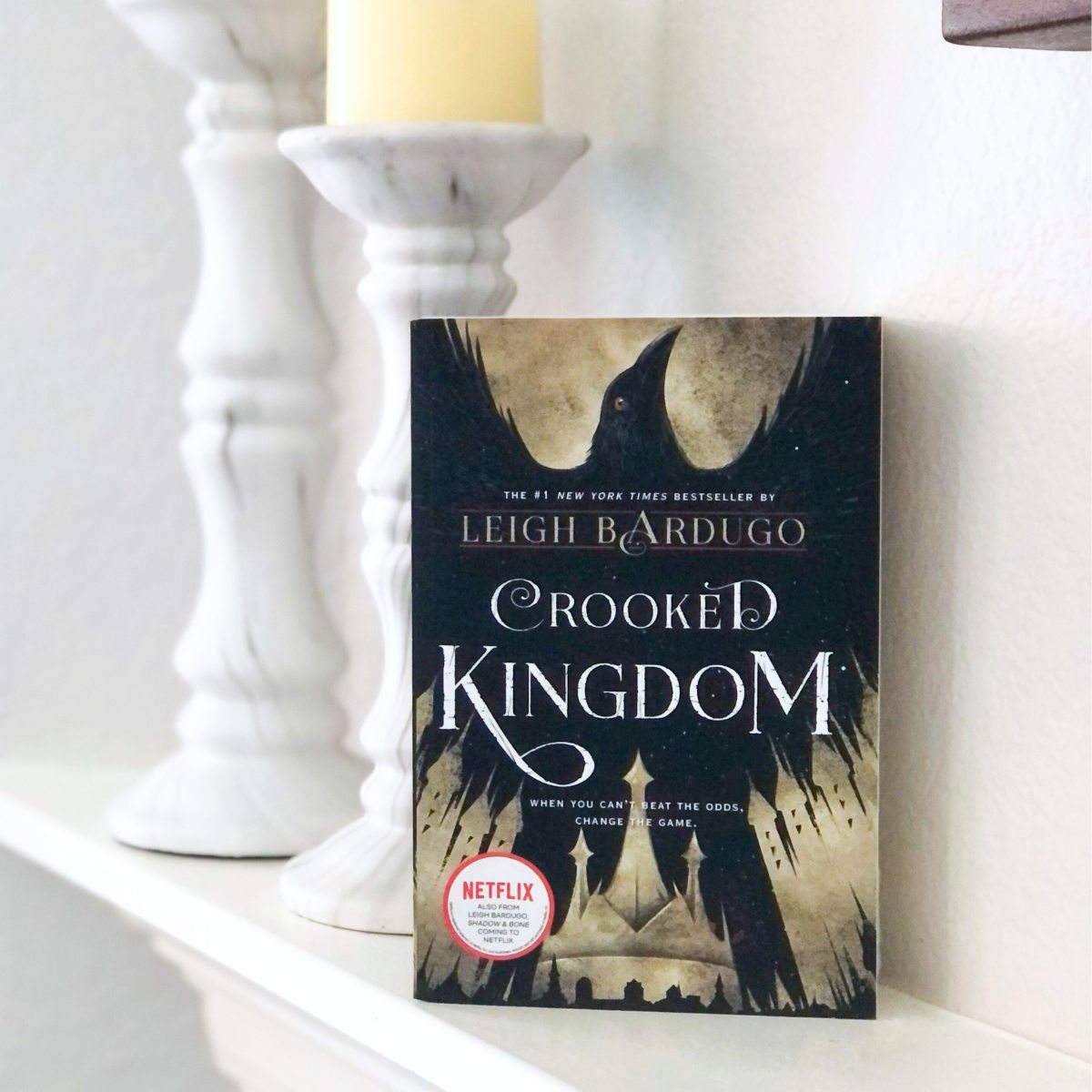 Crooked Kingdom paperback book on a white fireplace mantle with candles