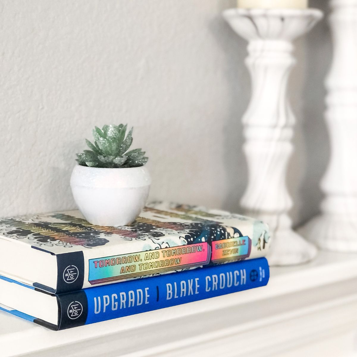 stack of hardcover books on a white fireplace mantel with a small plant on top