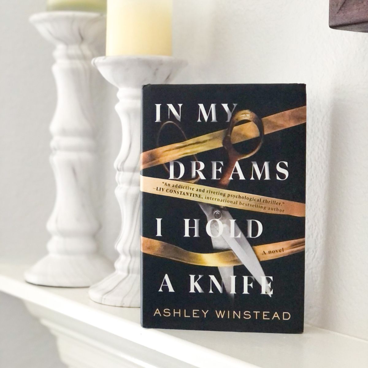 In My Dreams I Hold a Knife hardcover book by Ashley Winstead on a fireplace mantel with candles
