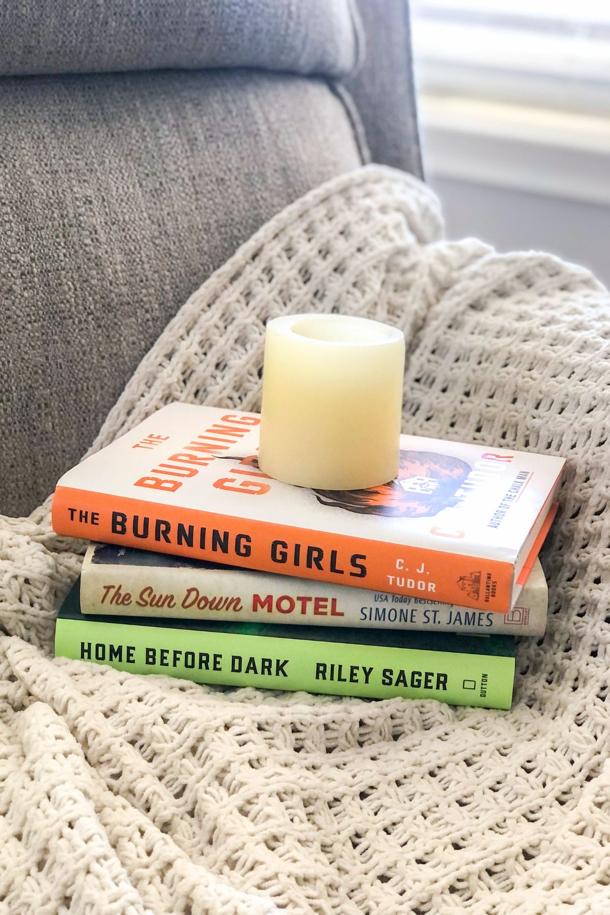 spooky mystery books with a candle stacked on a white blanket over a grey chair