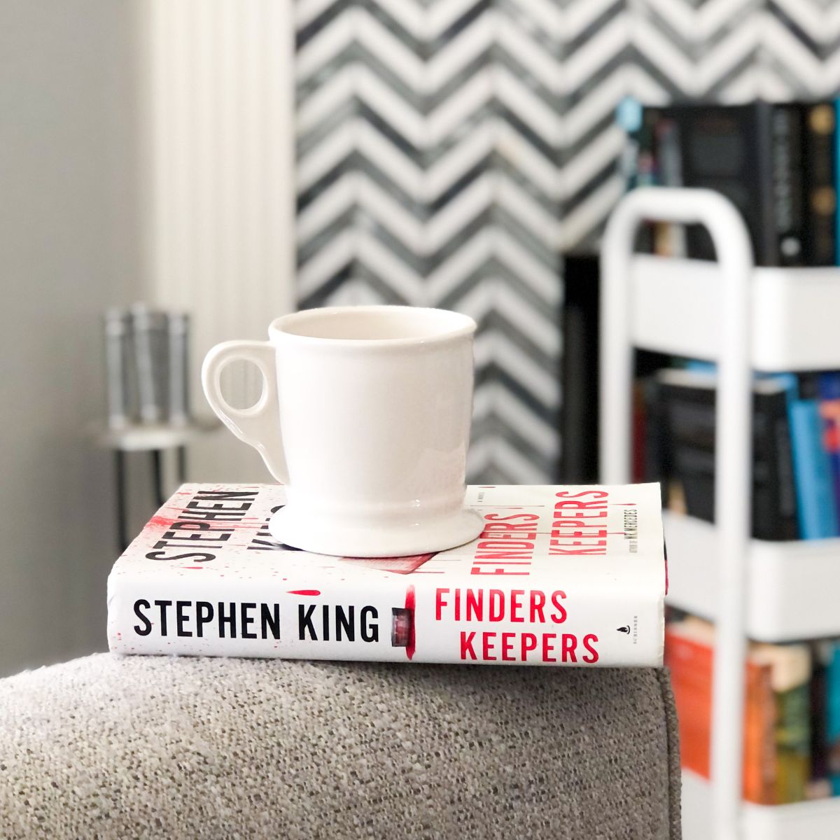 Stephen King hardcover mystery novel sitting on a grey chair with a coffee mug on top