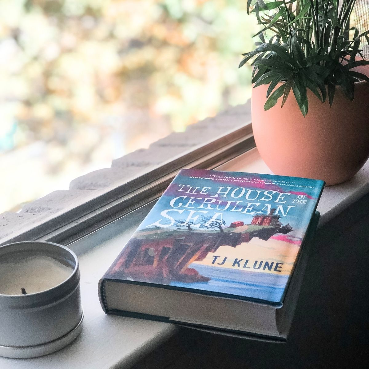 The House in the Cerulean Sea book sitting on a windowsill with a candle and a plant