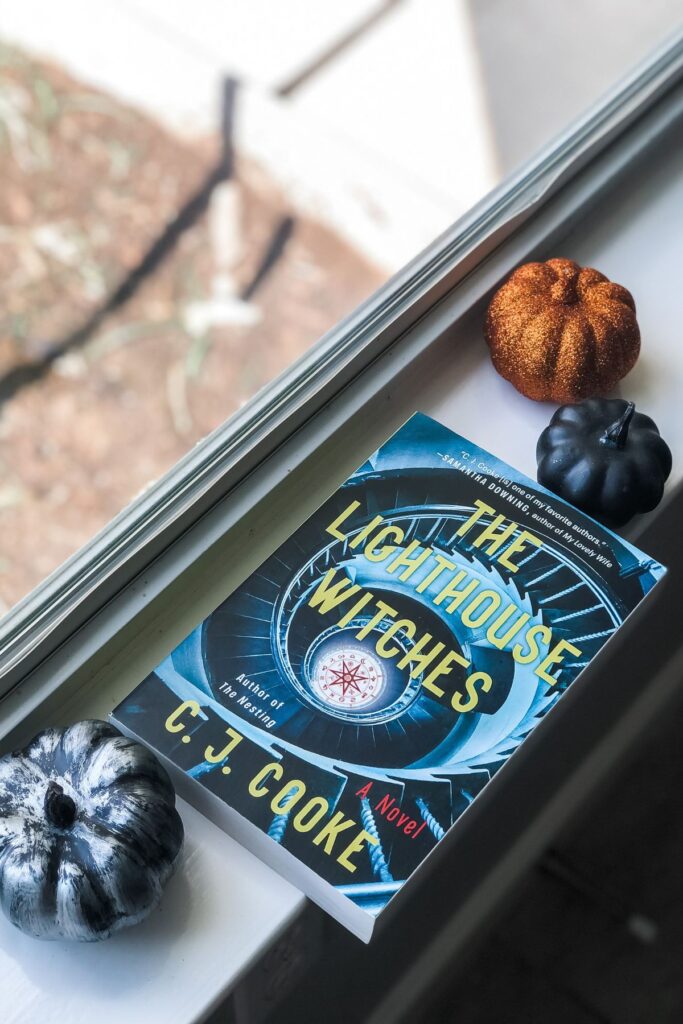 The Lighthouse Witches book sitting on a windowsill with mini pumpkins