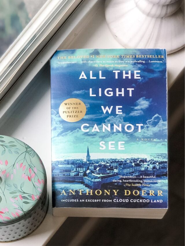 All The Light We Cannot See paperback book on a windowsill beside a candle