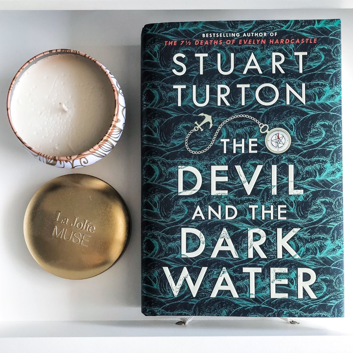 hardcover Stuart Turton book next to a white and gold candle